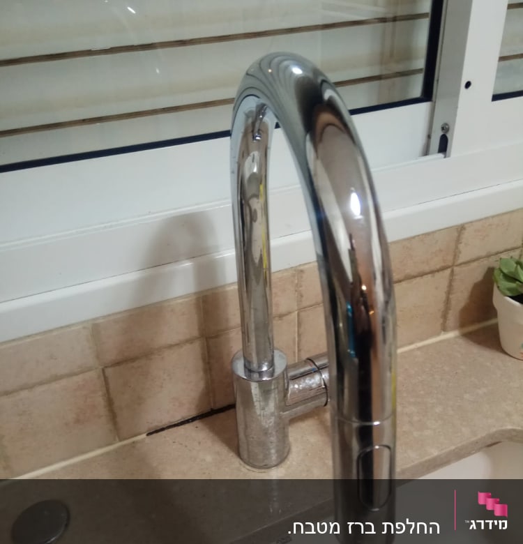 ברז מטבח כסוף על משטח שיש ליד חלון